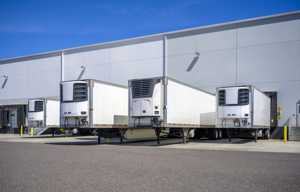 Industrial grade refrigerator semi trailers with reefer units on the front wall and without semi trucks standing at warehouse dock gates loading chilled and frozen cargo for next freight delivery"n
